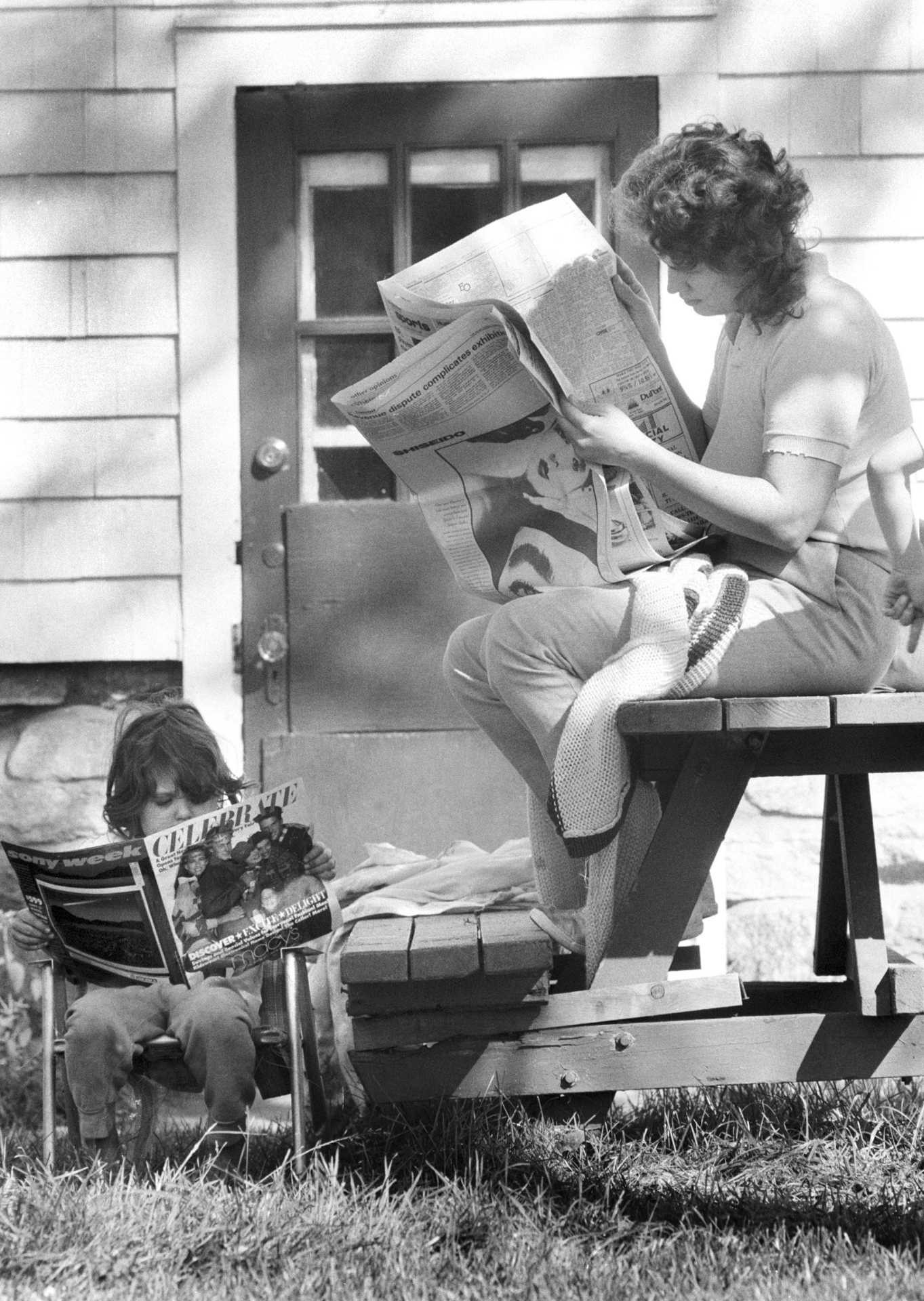 Mother and daughter read the paper outside on a warm October day. 1987